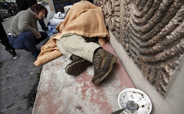 Una integrante de un servicio social de emergencias para gente sin hogar entrega un saco de dormir a un hombre sin techo./Reuters