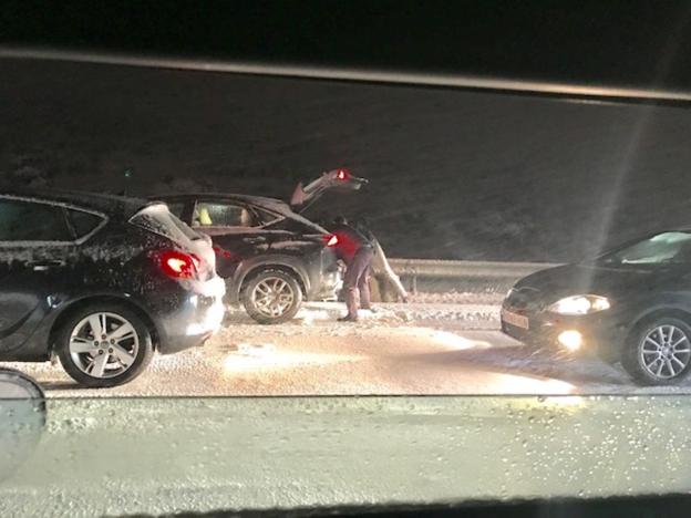 Dos personas buscan en el interior de su vehículo, apartado en un arcén de la autopista de peaje en plena noche, con la carretera llena de nieve. / JOSÉ VICENTE ALONSO