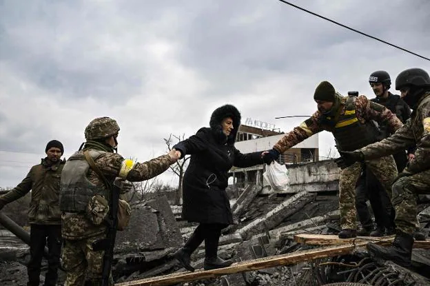 Los soldados ayudan a una mujer a cruzar sobre los escombros de un puente destruido a unos kilómetros de Kiev. / AFP